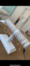 Close-up of sparkling gold chain and multicolored beaded bracelets draped on a white T-bar jewelry display on a wooden table