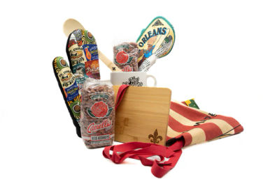 New Orleans–style kitchen gift set with wooden spoon, colorful potholders and spatula, coffee mug, bagged red kidney beans, bamboo cutting board, and striped apron.