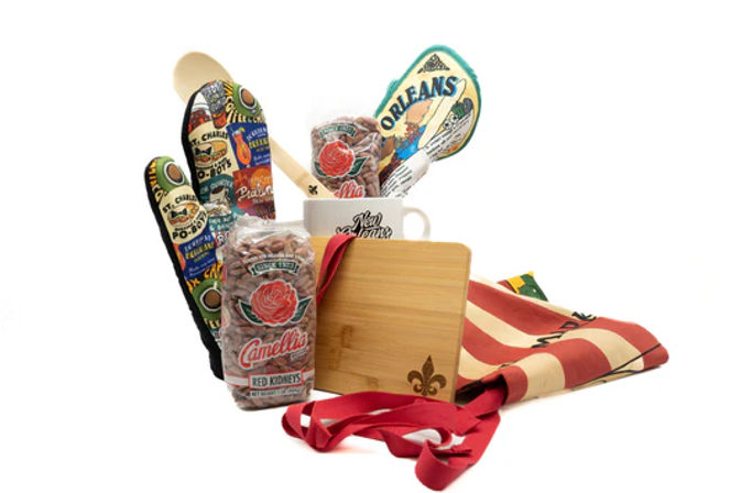 New Orleans–style kitchen gift set with wooden spoon, colorful potholders and spatula, coffee mug, bagged red kidney beans, bamboo cutting board, and striped apron.