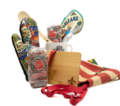 New Orleans–style kitchen gift set with wooden spoon, colorful potholders and spatula, coffee mug, bagged red kidney beans, bamboo cutting board, and striped apron.