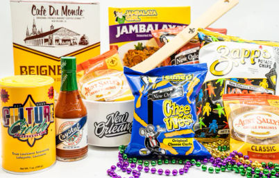 New Orleans–themed snack assortment with beignet mix, jambalaya rice mix, hot sauce, pralines, potato chips and cheese curls, wooden spoon and colorful Mardi Gras beads.