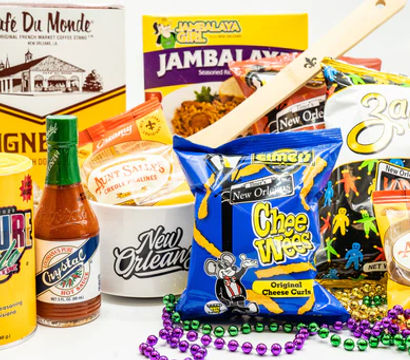 New Orleans–themed snack assortment with beignet mix, jambalaya rice mix, hot sauce, pralines, potato chips and cheese curls, wooden spoon and colorful Mardi Gras beads.