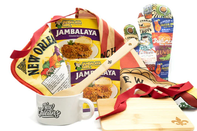 New Orleans–themed Cajun cooking set with jambalaya mix boxes, wooden spoon, coffee mug, cutting board, apron and colorful oven mitts.