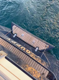 Top-down view of a yacht's aft teak swim platform and folding boarding step tied with ropes, set against rippling deep-blue sea — ready for a swim.