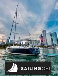 Sailboat with American flag anchored on Lake Michigan near the Chicago skyscraper skyline, paddleboards in the foreground and dramatic cloudy sky overhead.