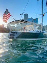 Sunlit sailboat sporting an American flag, bobbing on shimmering green water with a modern downtown skyline in the background.