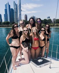 Eight friends in bikinis posing on a sailboat with the Chicago skyline and Lake Michigan in the background on a sunny summer day