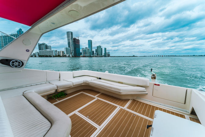 Yacht aft deck with white cushioned seating and teak-style flooring facing the Miami skyline across turquoise bay under a dramatic cloudy sky