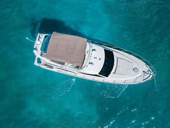 Aerial bird's-eye view of a white luxury motor yacht with tan canopy floating in clear turquoise tropical water