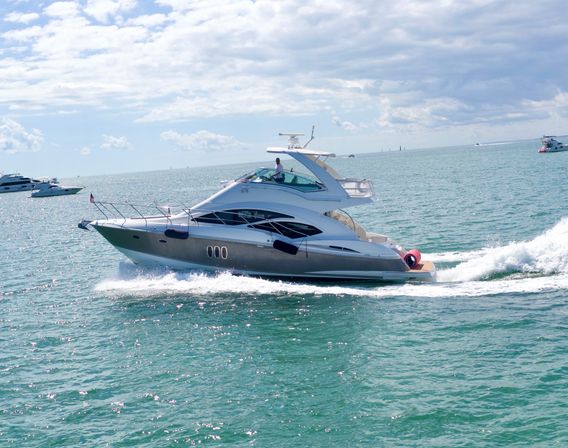 Sleek white luxury motor yacht cruising across turquoise open sea on a sunny, partly‑cloudy day, leaving a foamy wake