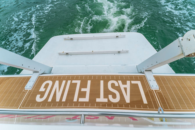 Aft yacht swim platform with playful "LAST FLING" lettering overlooking churning green sea water and wake