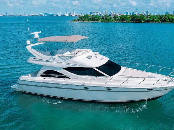 White luxury motor yacht cruising turquoise coastal waters near a green shoreline and harbor skyline on a sunny day