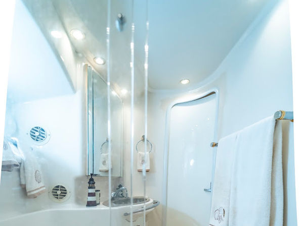 Compact white yacht bathroom with curved glass shower door, small sink and mirrored cabinet, porthole-style vents and towel rack — bright nautical head