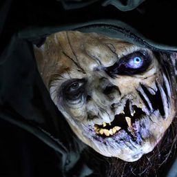 Close-up of a hooded, decayed witch-like horror prop with a glowing blue eye, yellow rotting teeth and torn mouth, spooky Halloween haunted-house decoration.