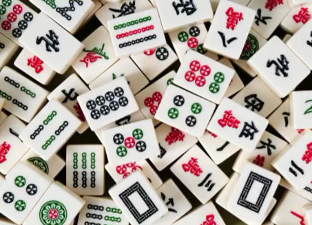 Close-up of a playful pile of Chinese mahjong tiles showing colorful circle, bamboo and character suit symbols on white game pieces.