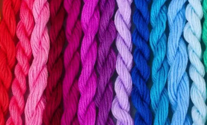 Close-up of twisted embroidery floss arranged in a rainbow gradient from red through pink, purple, blue to teal