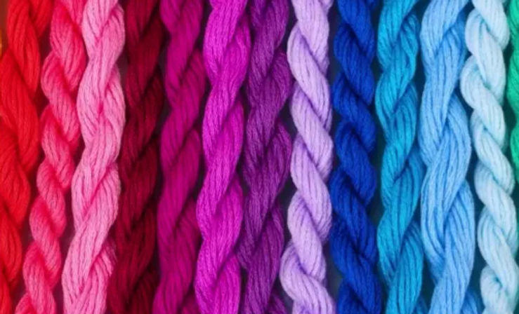 Close-up of twisted embroidery floss arranged in a rainbow gradient from red through pink, purple, blue to teal