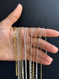 Hand holding assorted gold and silver chain necklaces draped over fingers against a black background, mixed-metal delicate and chunky chain styles close-up