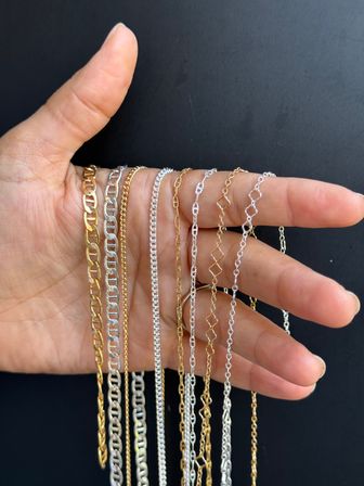 Hand holding assorted gold and silver chain necklaces draped over fingers against a black background, mixed-metal delicate and chunky chain styles close-up