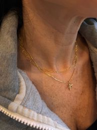 Close-up of a neck wearing layered gold necklaces, one with a small angel pendant, over a gray zip-up hoodie.