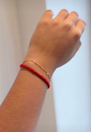 Close-up of a wrist wearing a braided red string bracelet and a delicate gold floral chain on a neutral background