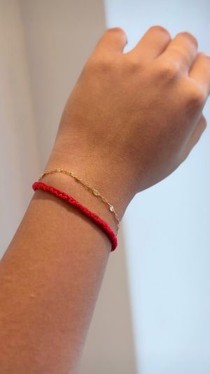 Close-up of a wrist wearing a braided red string bracelet and a delicate gold floral chain on a neutral background