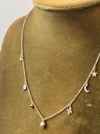 Silver charm necklace featuring a heart, small green heart, four-leaf clover, letter N, crescent moon and star draped on a brown velvet jewelry bust