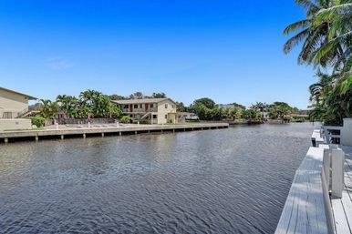 Sunny tropical waterfront canal with palm trees, low-rise waterfront condos and a white wooden dock under a clear blue sky.