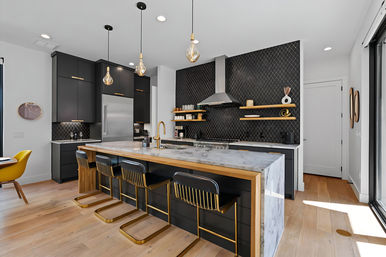 Contemporary open-concept kitchen with matte black cabinets, patterned tile backsplash, marble waterfall island, gold-accented bar stools and pendant lights on light hardwood floors.