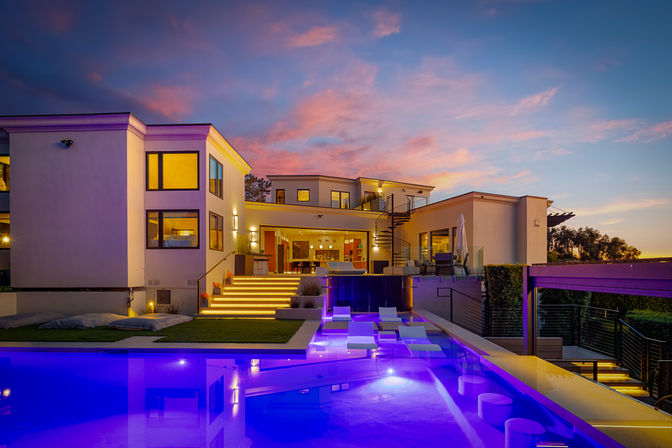 Modern luxury hillside home at sunset — glowing steps, spiral staircase, rooftop terrace and vivid blue LED infinity pool with submerged loungers.