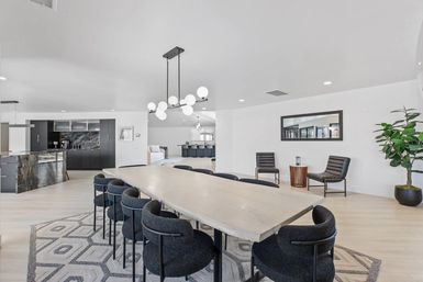 Modern open-concept dining area in a luxury home with a long light-wood table, black upholstered chairs on a geometric rug, globe chandelier, dark marble kitchen island, seating nook and potted plant