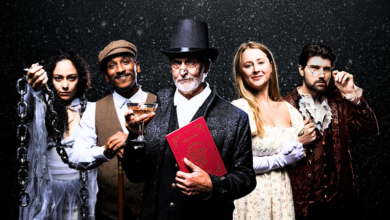 Victorian holiday theater cast portrait — five actors in period costumes: a Scrooge-like man in a top hat holding a red 'A Christmas Carol' book and glass, a ghost draped in chains, and three companions against a snowy studio backdrop.