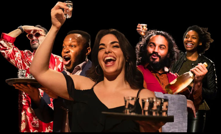 Group of five people cheering at a lively bar night, woman front-center holding a tray of shot glasses while others raise shots and a champagne bottle, smiling and celebrating.