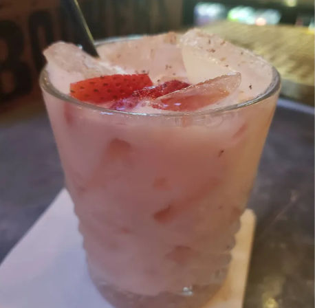 Iced pink strawberry cocktail in a short glass with ice cubes and sliced strawberries, served on a napkin at a dim bar or restaurant table