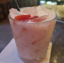 Refreshing pink strawberry cocktail with crushed ice and sliced strawberry in a short rocks glass on a napkin at a bar