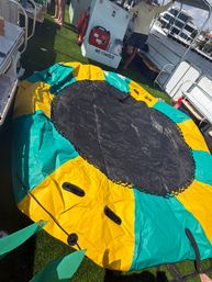 Colorful yellow-and-teal inflatable towable tube with a black center resting on a pontoon boat's artificial-grass deck at a waterfront marina, ready for tubing.