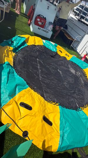 Colorful yellow-and-teal inflatable towable tube with a black center resting on a pontoon boat's artificial-grass deck at a waterfront marina, ready for tubing.