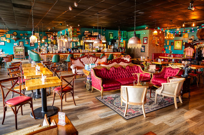Vibrant vintage café interior with a marble-front bar and green stools, plush red velvet sofas, wooden tables, eclectic retro decor and warm pendant lighting for a cozy urban lounge vibe.