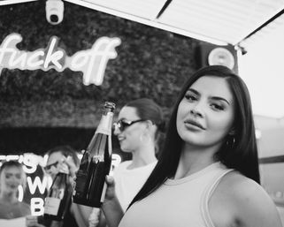 Black-and-white rooftop party scene: women toasting with champagne bottles under a neon "fuck off" sign — stylish nightlife photo.