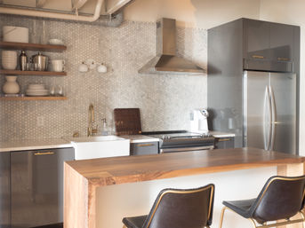 Sleek modern kitchen with hexagon marble backsplash, stainless steel appliances, farmhouse sink, brass faucet, walnut island and leather bar stools