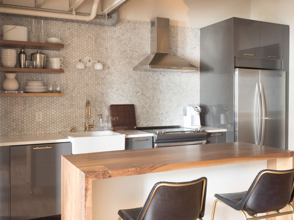 Sleek modern kitchen with hexagon marble backsplash, stainless steel appliances, farmhouse sink, brass faucet, walnut island and leather bar stools