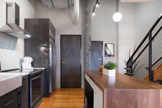 Sleek modern loft kitchen with a walnut island, stainless steel fridge and range, farmhouse sink, exposed beam and metal staircase
