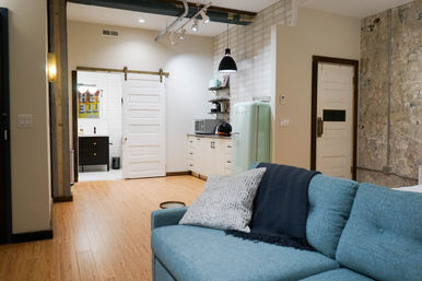 Industrial-chic urban loft studio with teal sofa and throw, bamboo floors, mint retro refrigerator, white subway-tiled kitchenette, sliding barn door, and exposed concrete accent wall.