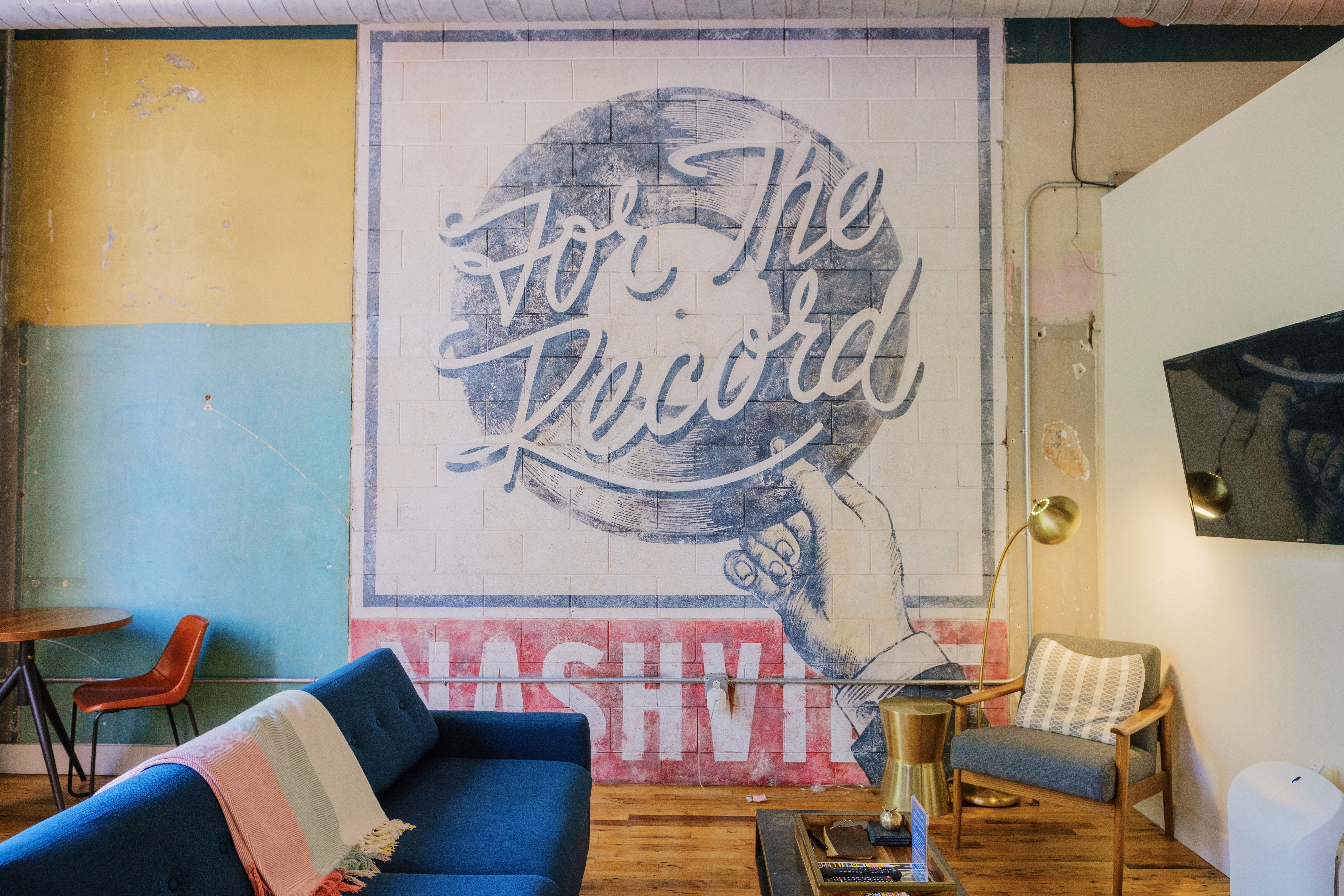 Colorful Nashville loft lounge with giant 'For The Record' mural, blue sofa, mid-century armchair and wooden floors.