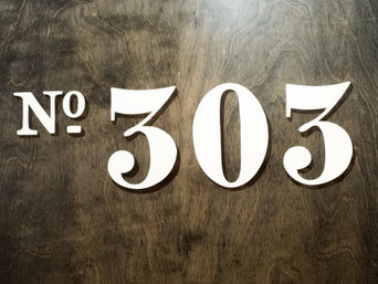 Stylish white 'No. 303' room number sign mounted on a dark stained wooden door