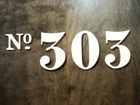 Stylish white 'No. 303' room number sign mounted on a dark stained wooden door