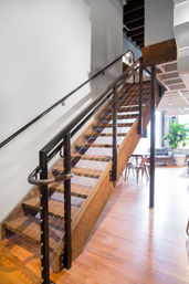 Sunlit industrial-style wooden staircase with metal cable railing and hardwood floors in a bright modern loft interior