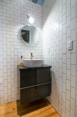 Compact modern powder room with white subway tile, round mirror, vessel sink on a dark floating vanity, brass faucet, wall sconce and warm wood floor