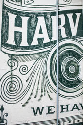 Vintage-style green mural on a white brick wall featuring large decorative letters (partial "HARV"), ornate swirls and concentric rings, with a vertical metal conduit running down the center.