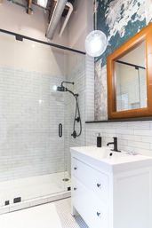 Urban loft bathroom with glass walk-in shower, white subway tile, matte-black shower fixtures, white vanity, leather-framed mirror and exposed industrial ceiling